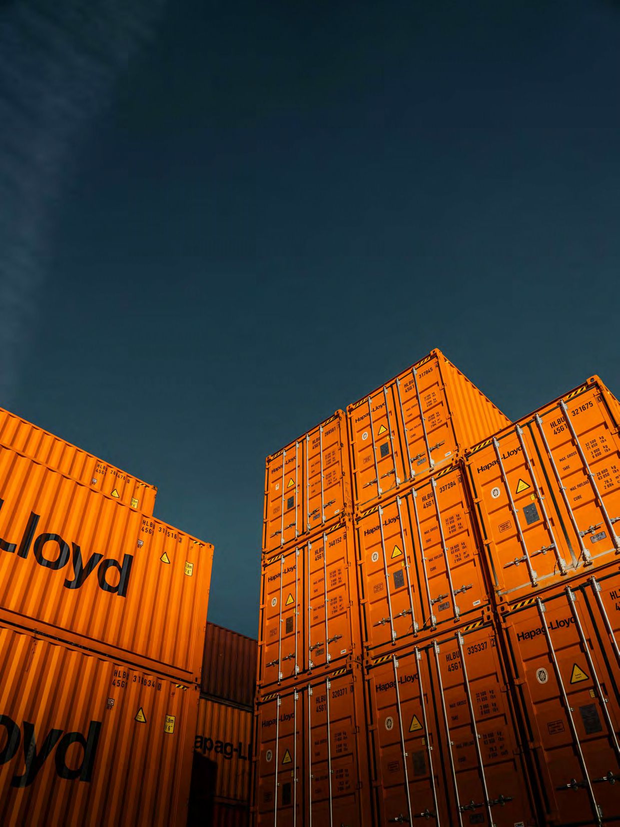 Stacked orange shipping containers under dark sky.